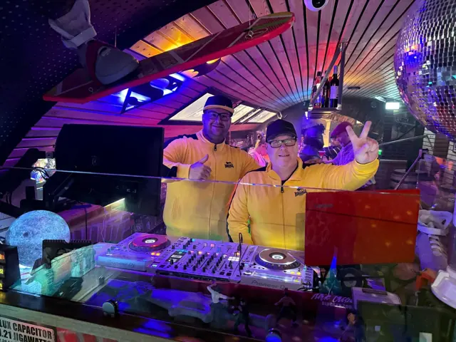 Zwei DJs in gelben Shirts am DJ-Pult der Bar Zeitreise in Celle