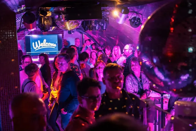 Partynacht: tanzende Gäste in pinkem Licht unter Discokugeln in der Bar Zeitreise Celle